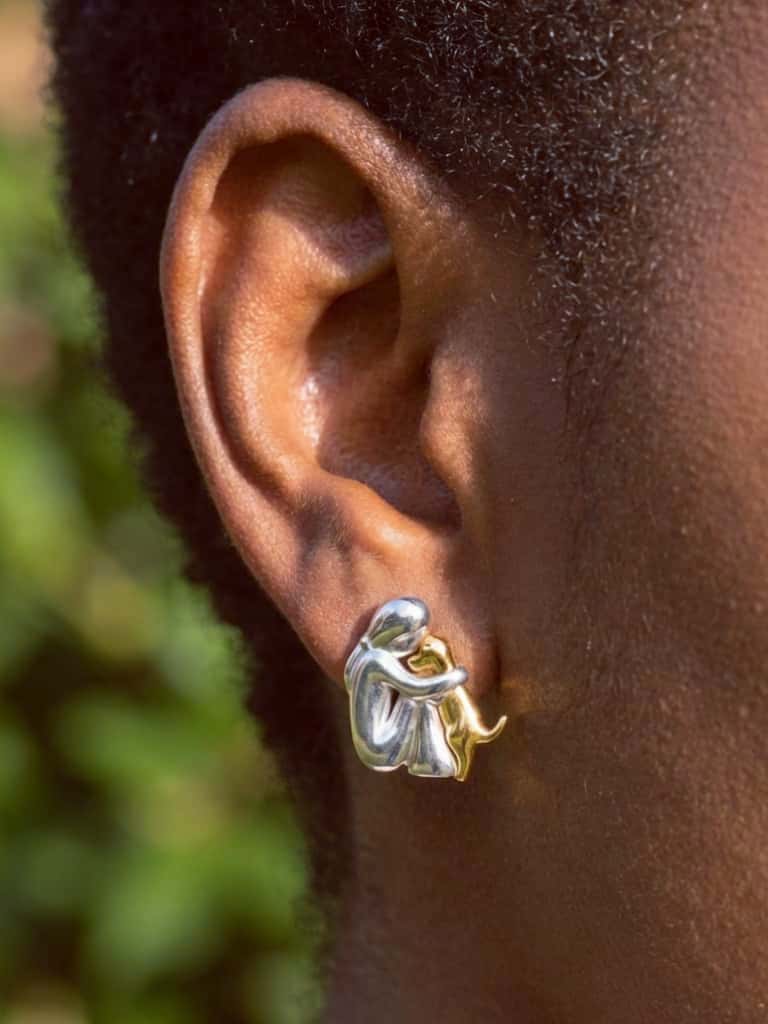Close-up of an ear wearing a gold and silver god huge earring with a blurred green background