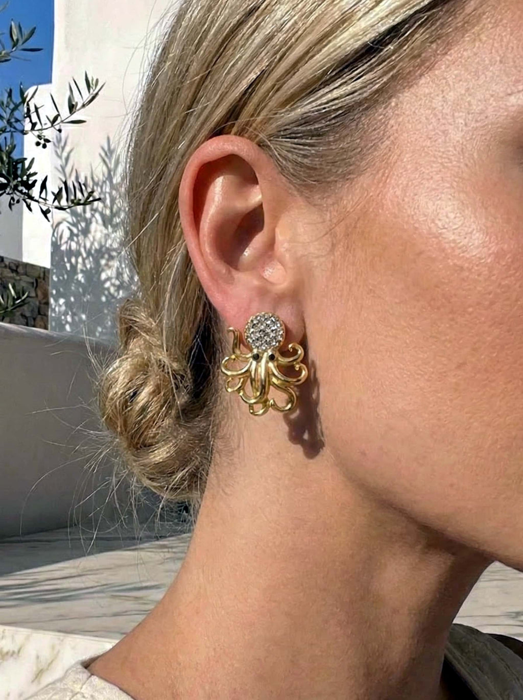 Close-up of a person wearing gold octopus earrings with a blurred outdoor background