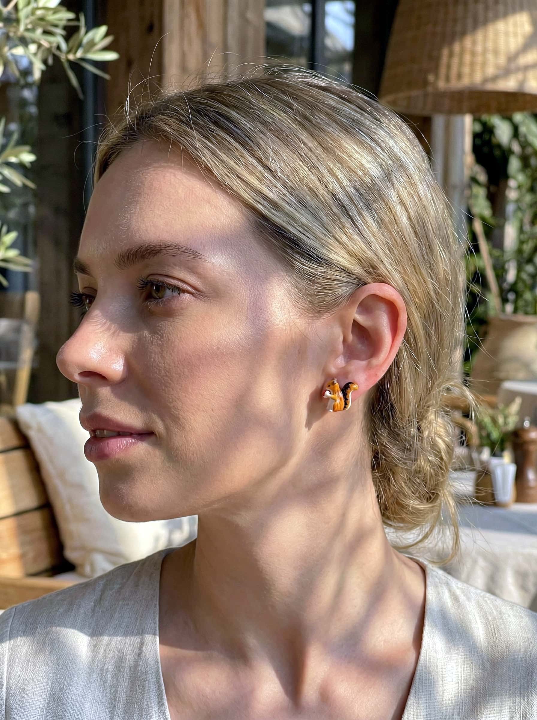 Woman wearing squirrel earrings with a blurred outdoor background
