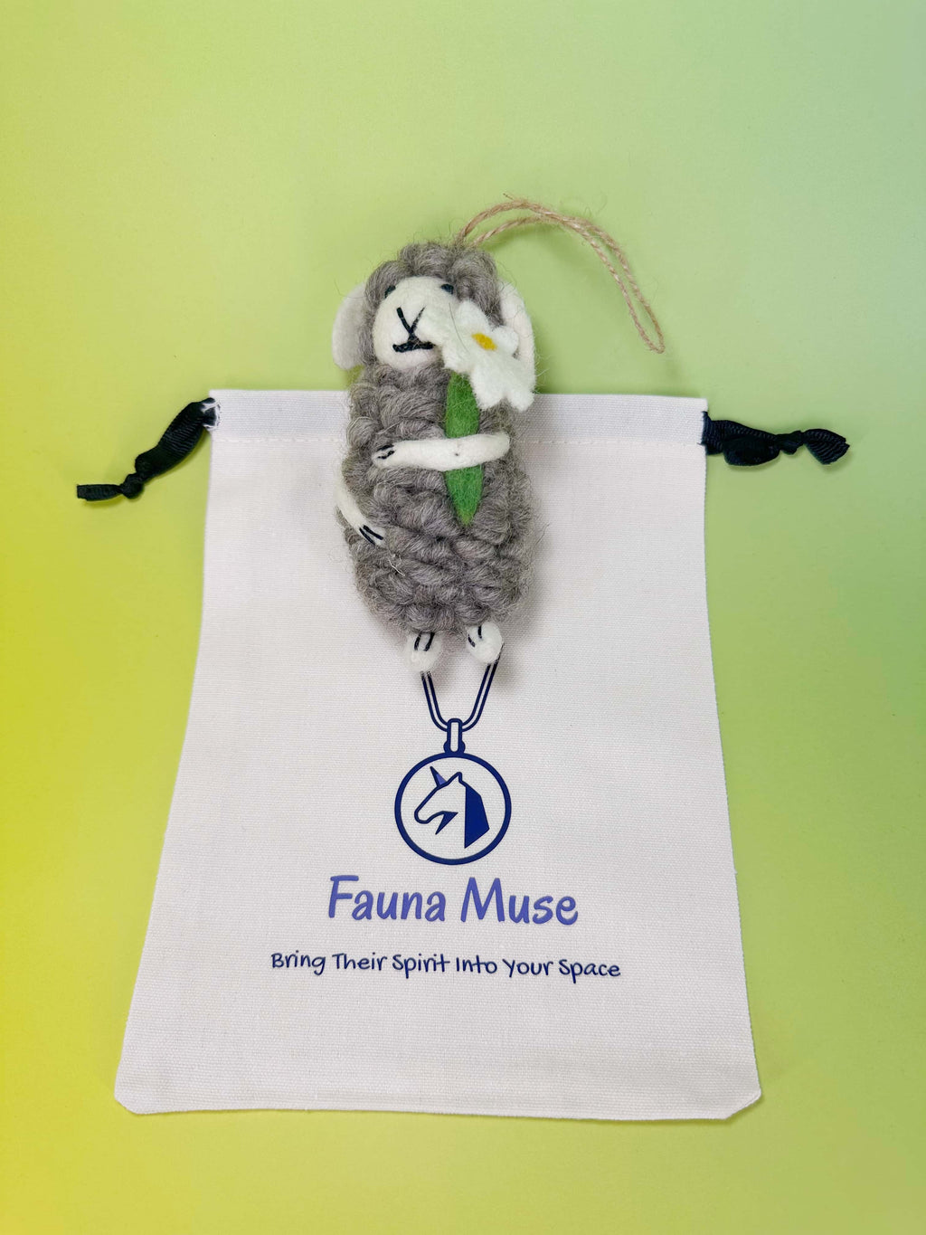 Handmade needle felted grey wool sheep ornament holding a white daisy flower with Fauna Muse gift pouch