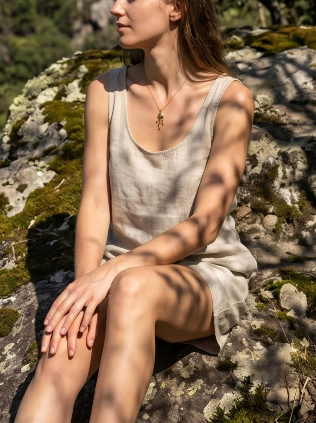 Elegant ocean necklace with a detailed jellyfish pendant worn by a model sitting on a mossy rock in a serene, vintage nature setting