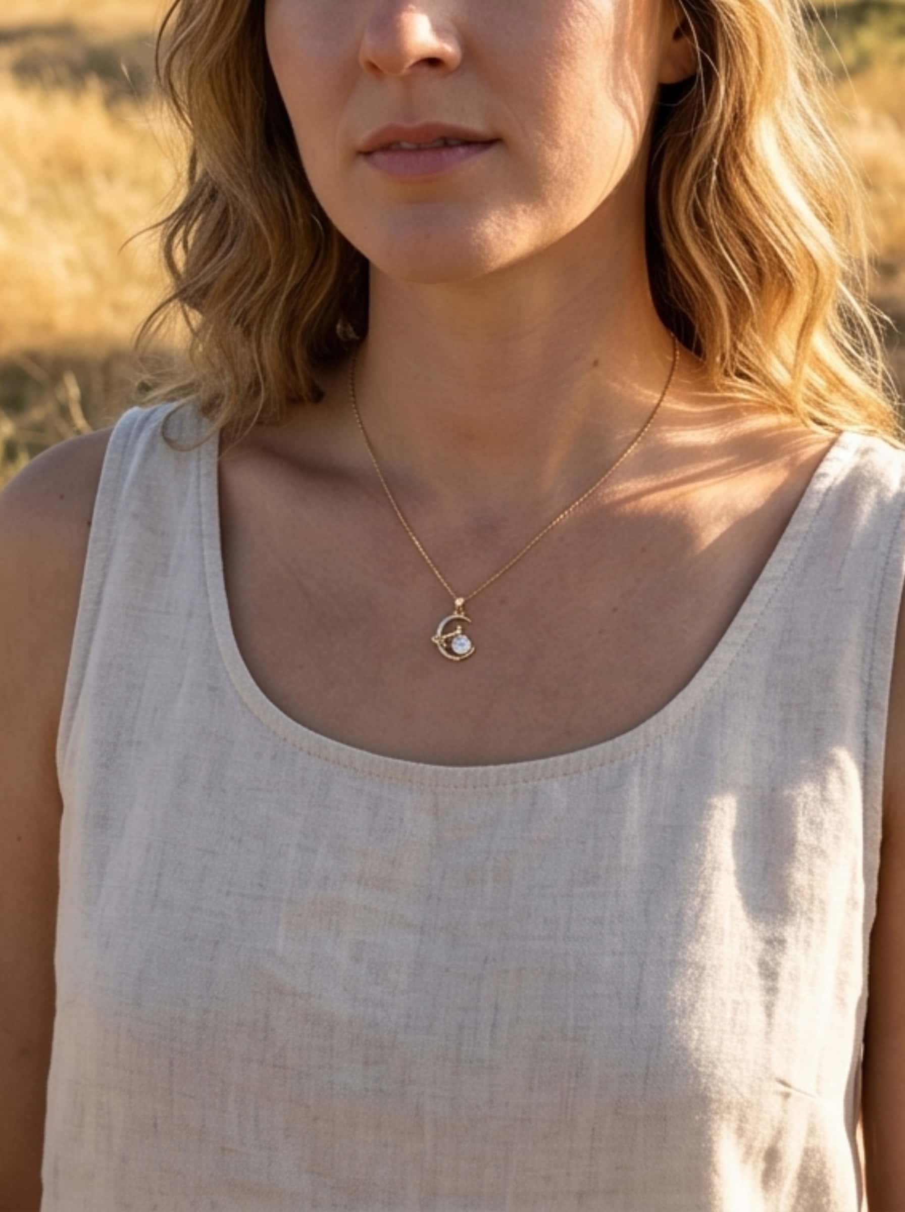 A model wearing an organic modern linen tank top showcases the minimalist cat necklace for women against a soft, golden hour outdoor background