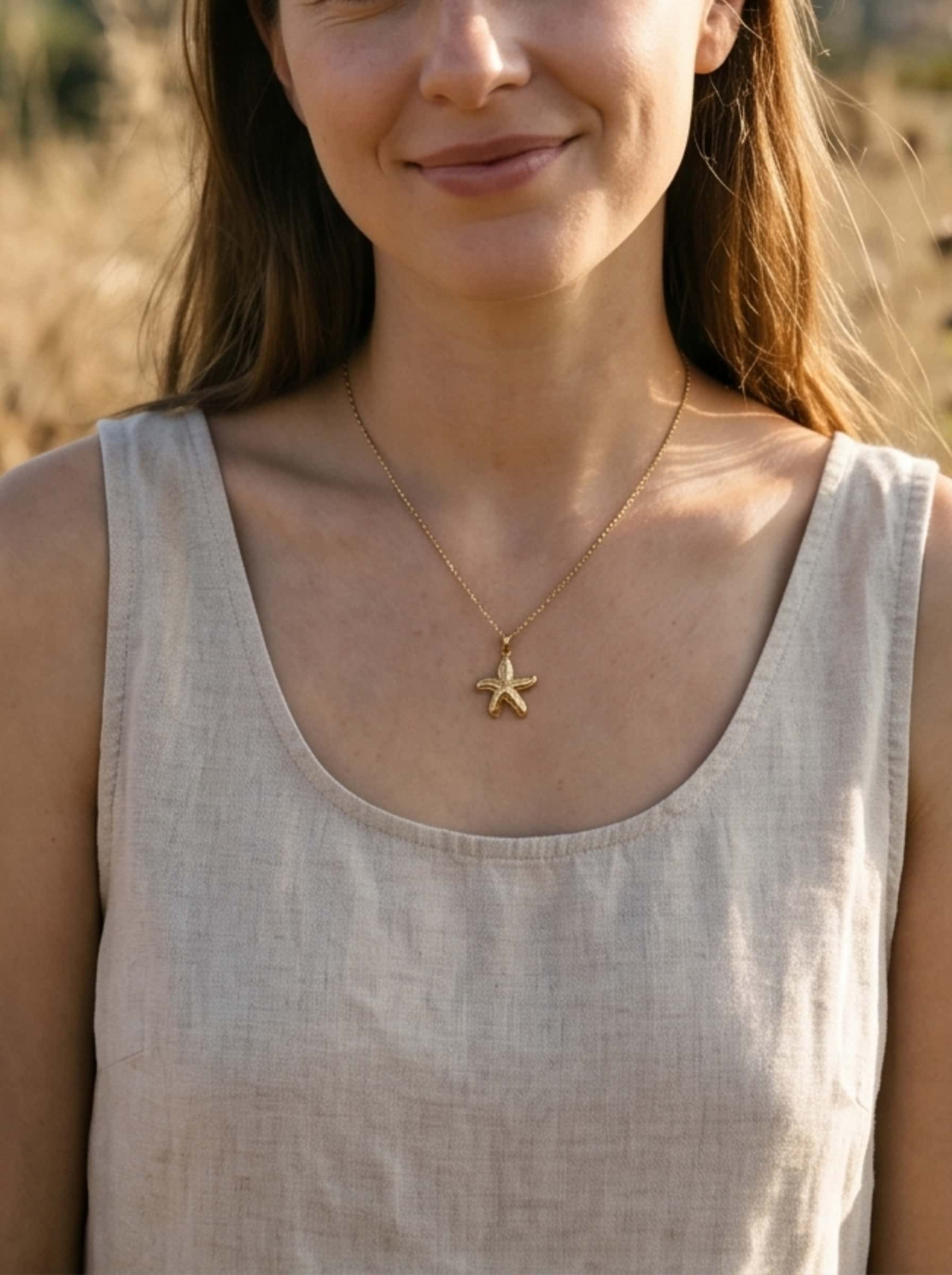 A woman in a natural linen dress wearing a dainty gold starfish necklace during a warm, sun-drenched outdoor lifestyle shoot