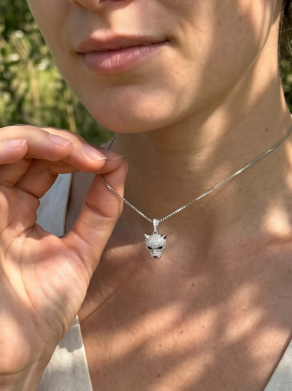 A woman in a natural linen top gently holding the delicate leopard necklace pendant, styled in warm, dappled sunlight for a vintage nature aesthetic