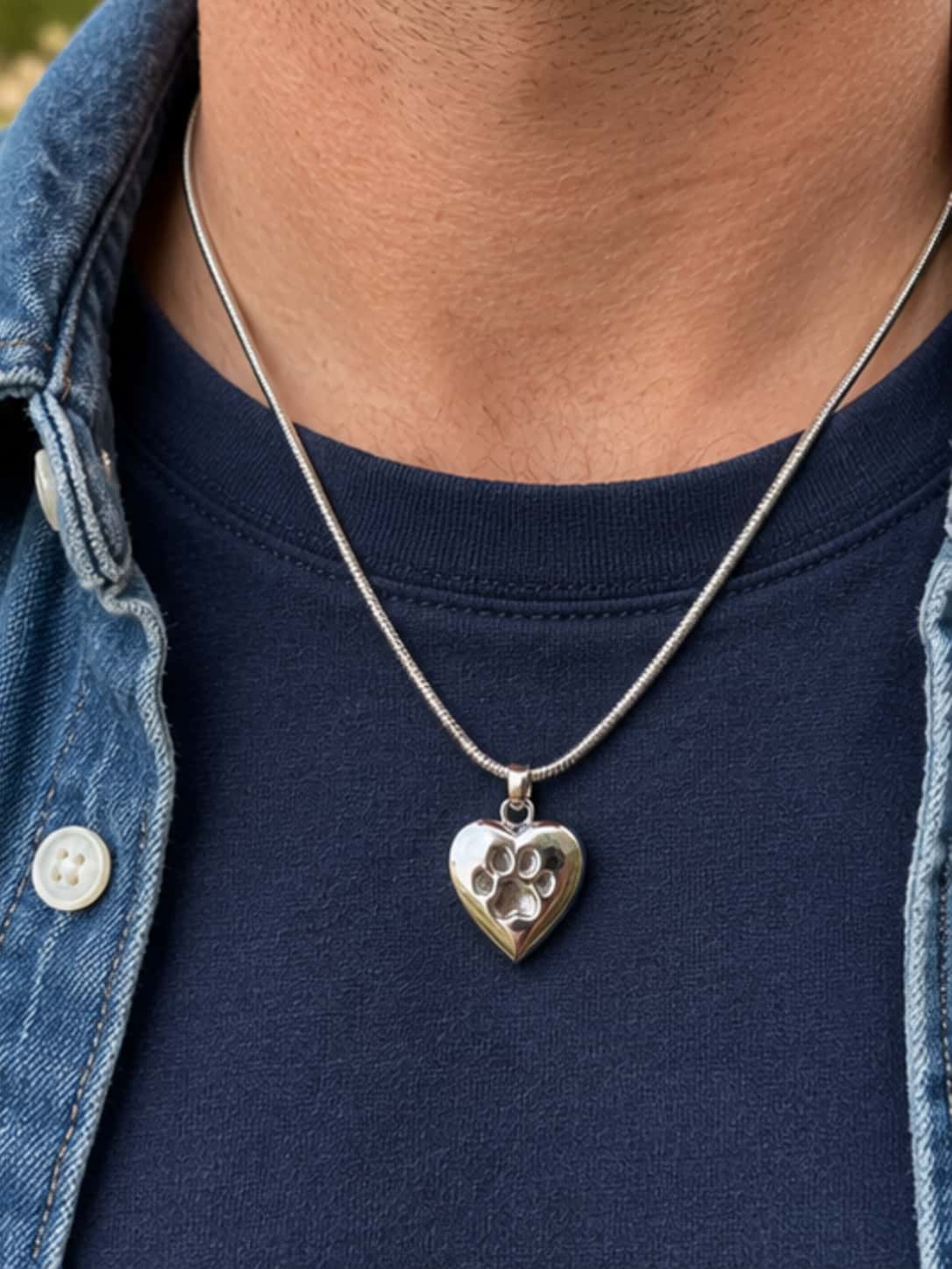 Close-up of a polished paw print heart necklace urn worn over a man's navy T-shirt