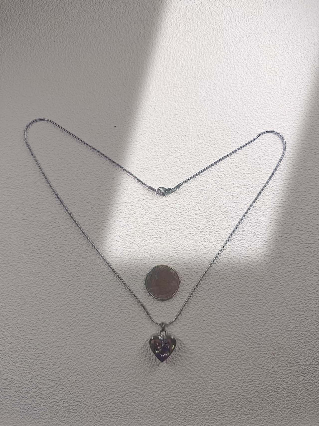 Paw print heart pet urn necklace laid flat beside a coin for scale, with the full chain and clasp visible