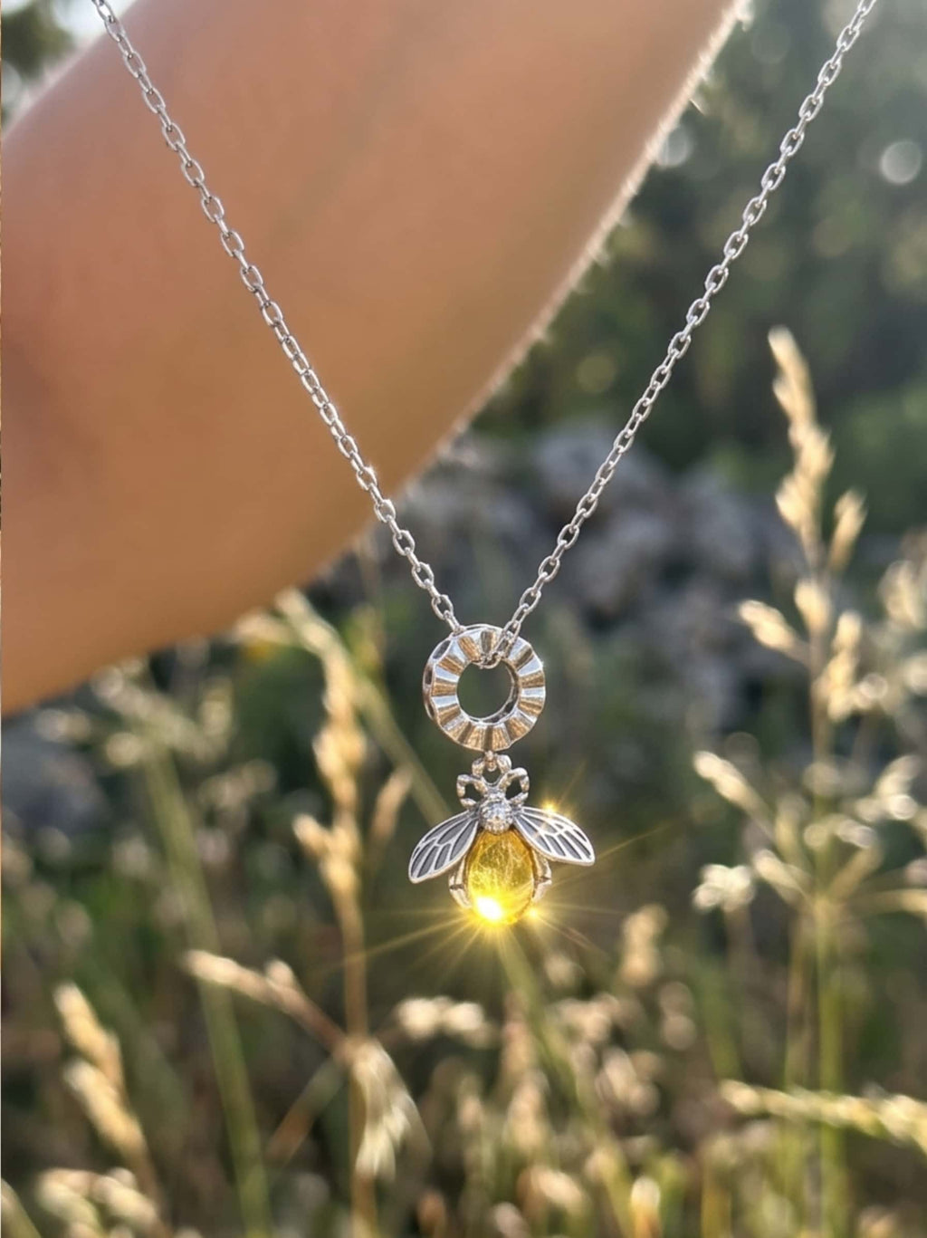 A dazzling gold bee necklace alternative crafted in sterling silver, held up to catch the sunlight, creating a bright optical flare on the yellow crystal abdomen
