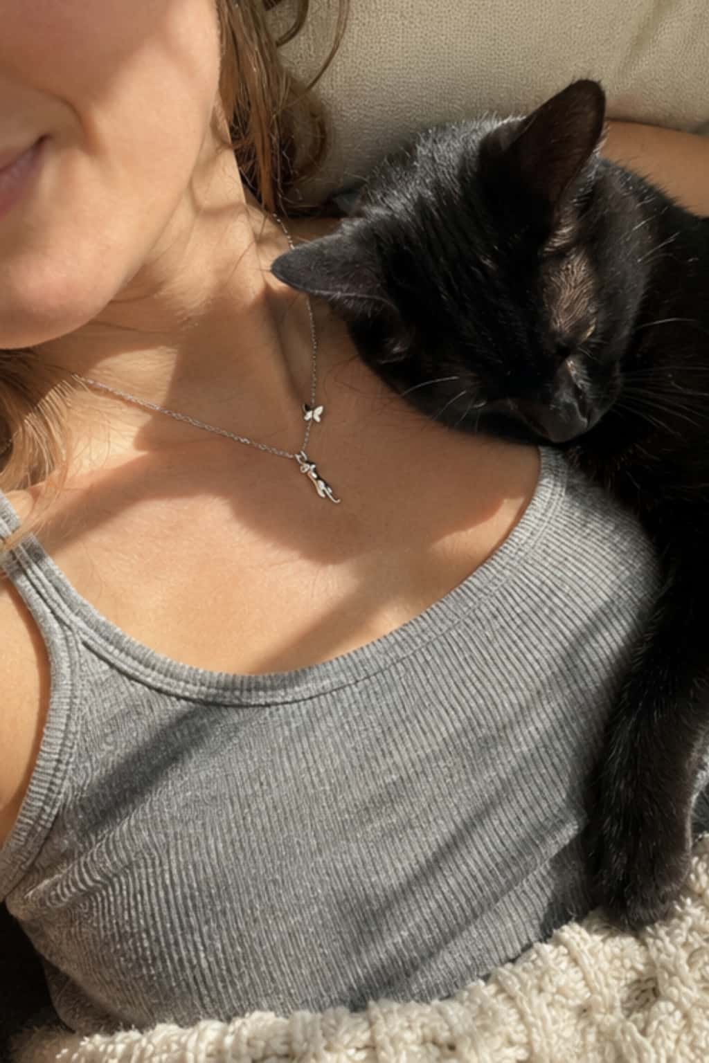 Woman wearing an S925 sterling silver hanging cat necklace with butterfly charm beside a sleeping black cat