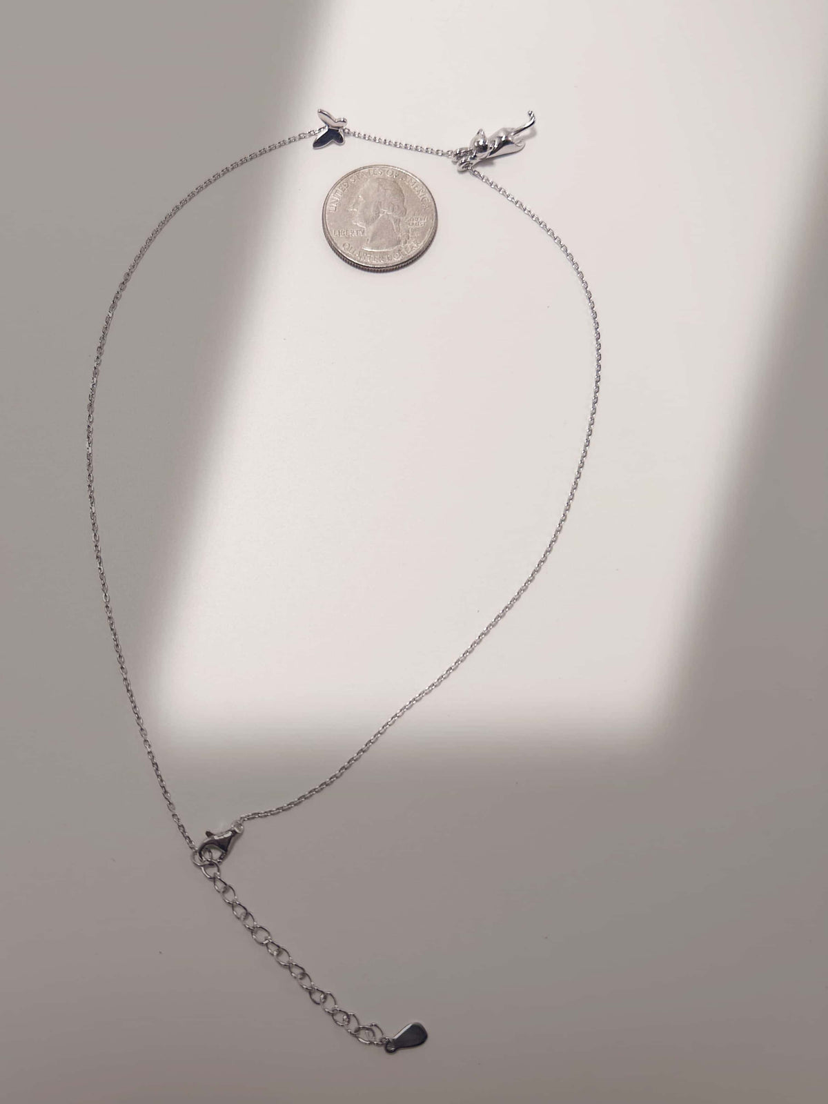 S925 sterling silver cat and butterfly pendant necklace laid flat next to a US quarter for size and scale comparison