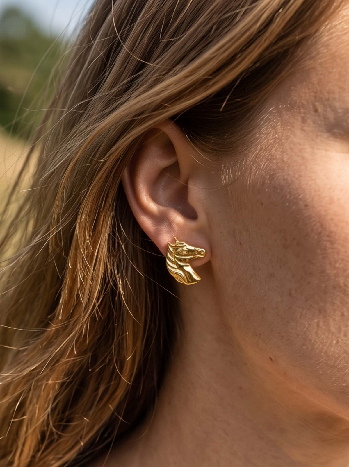 Side profile view of a woman wearing gold equestrian horse earrings outdoors