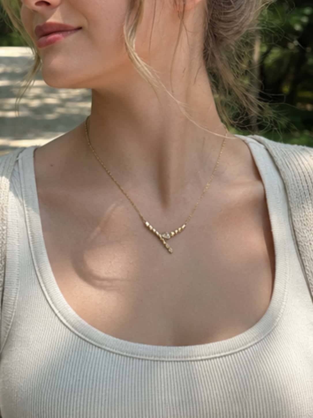 Profile view of a woman highlighting the minimalist serpent necklace in gold, catching natural sunlight to show the brilliant texture