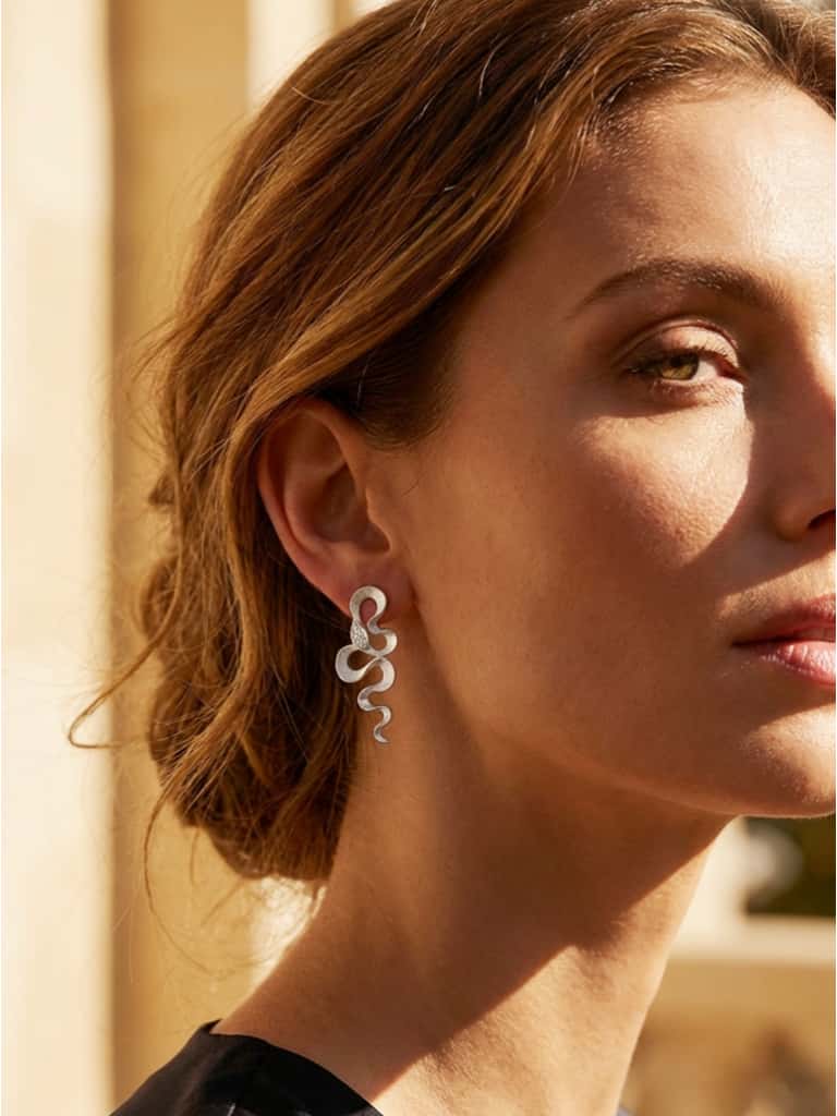 Close-up of a woman wearing snake earrings with a blurred background