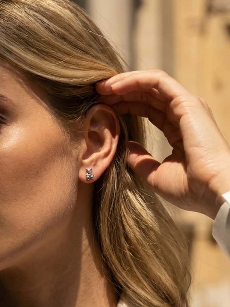 Close-up of a woman wearing a small silver teddy bear earring with a blurred background