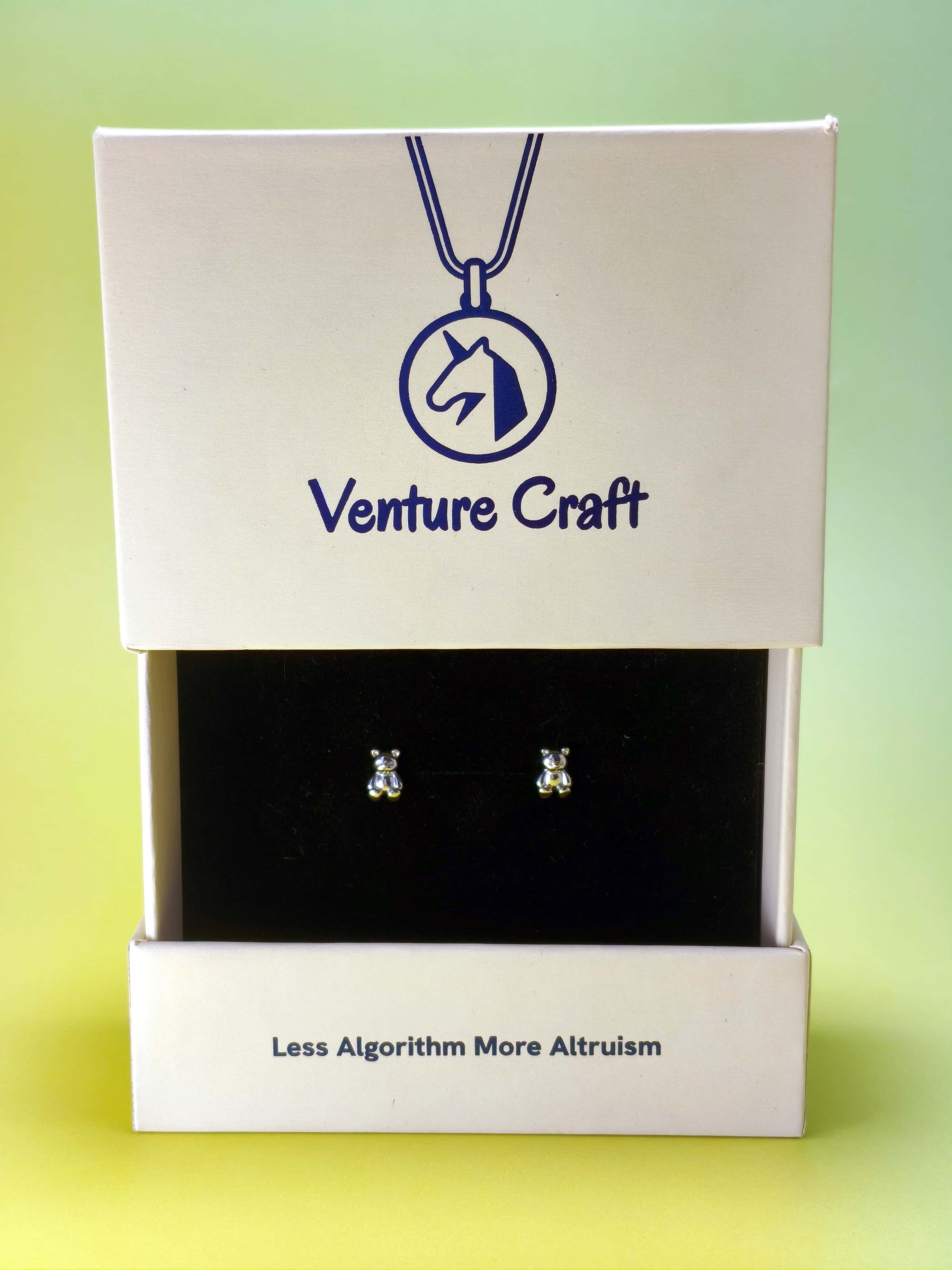 Silver teddy bear earrings in a 'Venture Craft' gift box on a gradient background