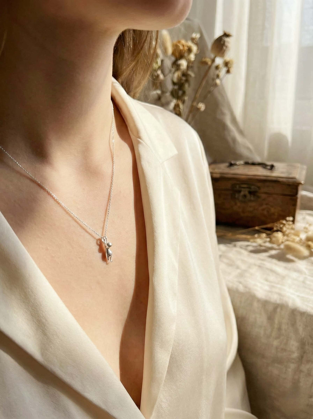 model wearing a cat pendant in a softly lit room.