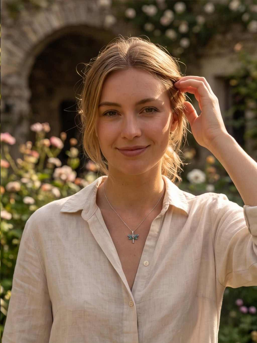 A smiling blonde woman in a garden setting wearing a beautiful sterling silver dragonfly necklace, showcasing it as an elegant everyday jewelry piece