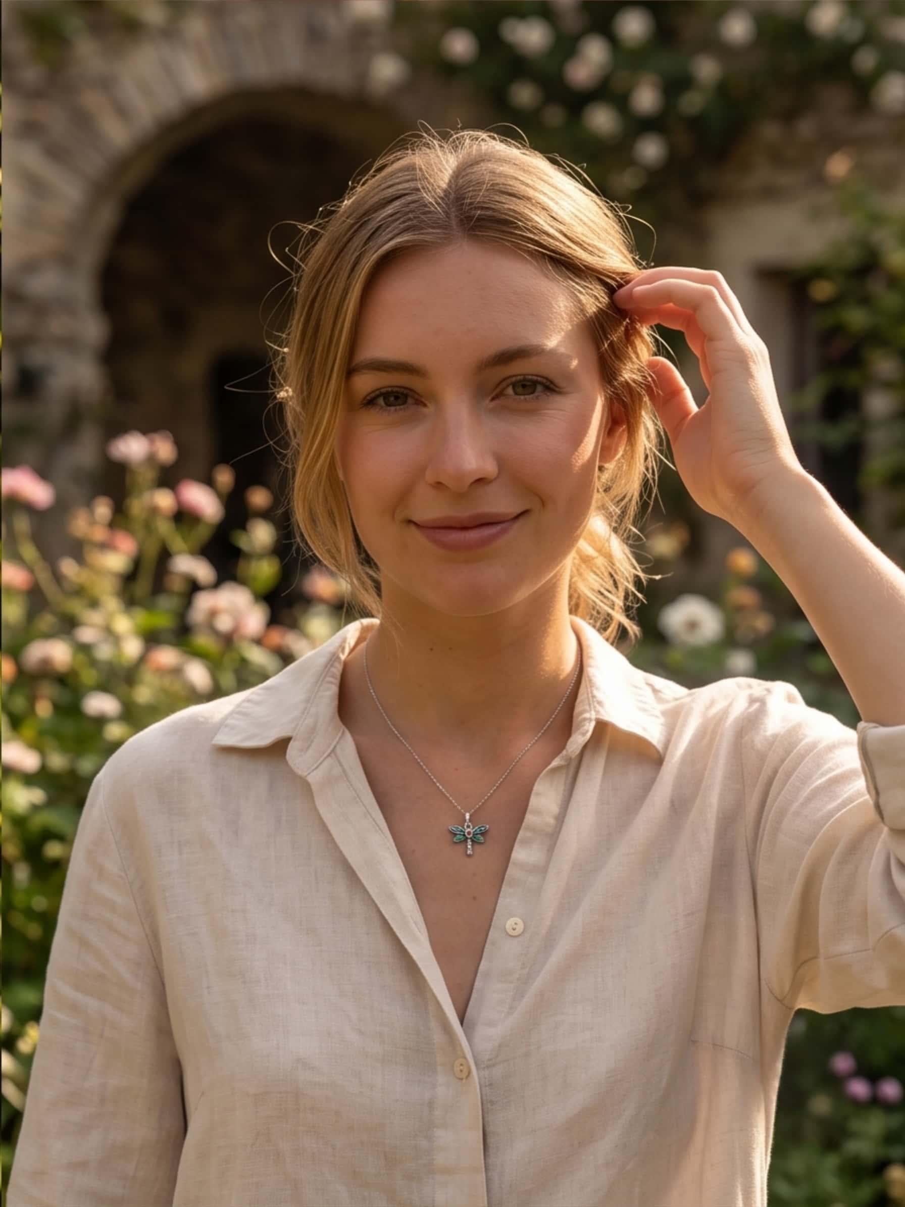 A smiling blonde woman in a garden setting wearing a beautiful sterling silver dragonfly necklace, showcasing it as an elegant everyday jewelry piece