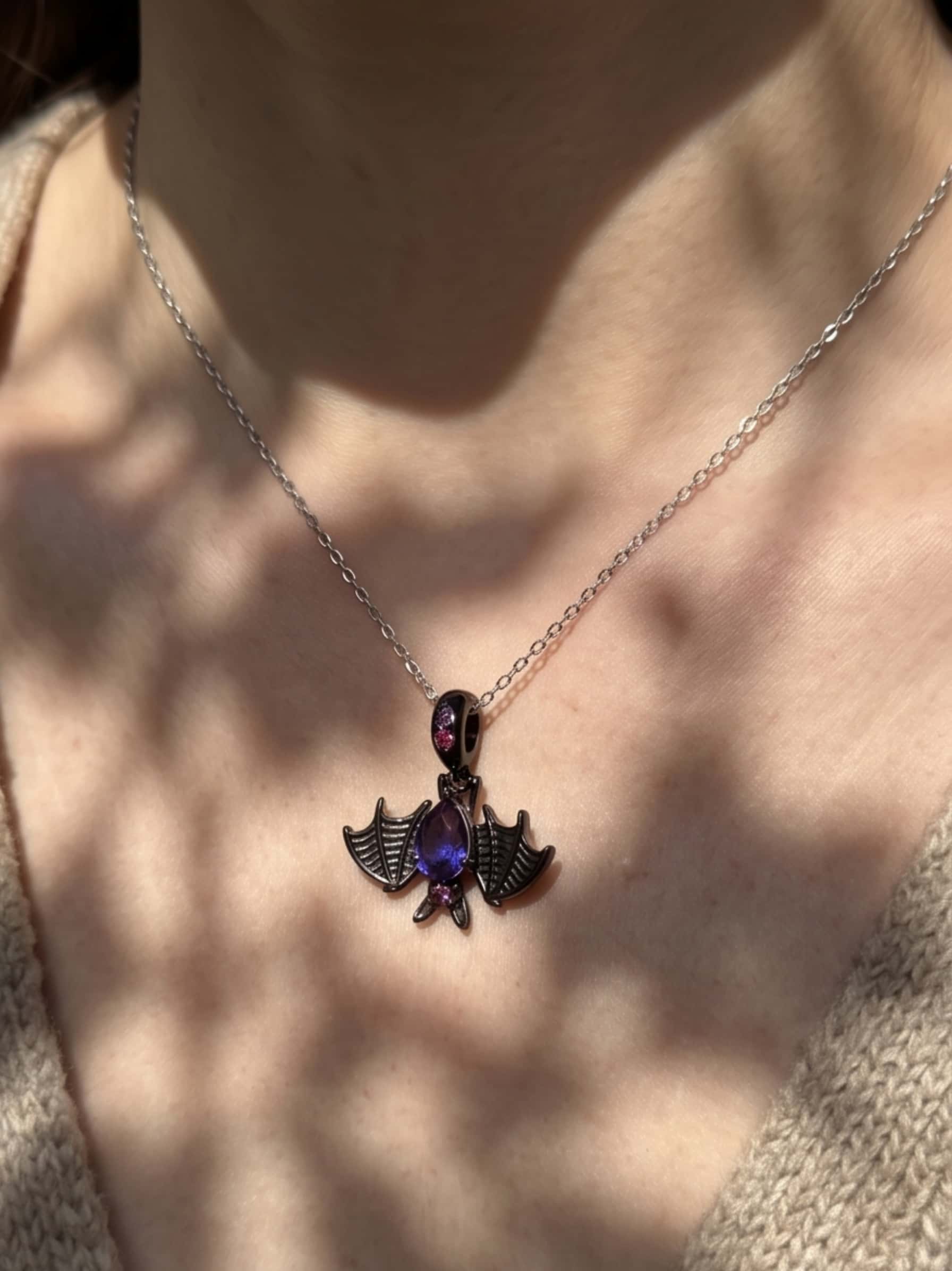 Dappled sunlight shining on a bat necklace silver pendant worn with a cozy beige knit sweater