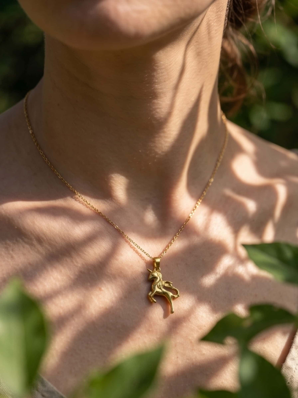 Aesthetic close-up of the unicorn necklace worn outdoors, highlighted by natural dappled leaf shadows