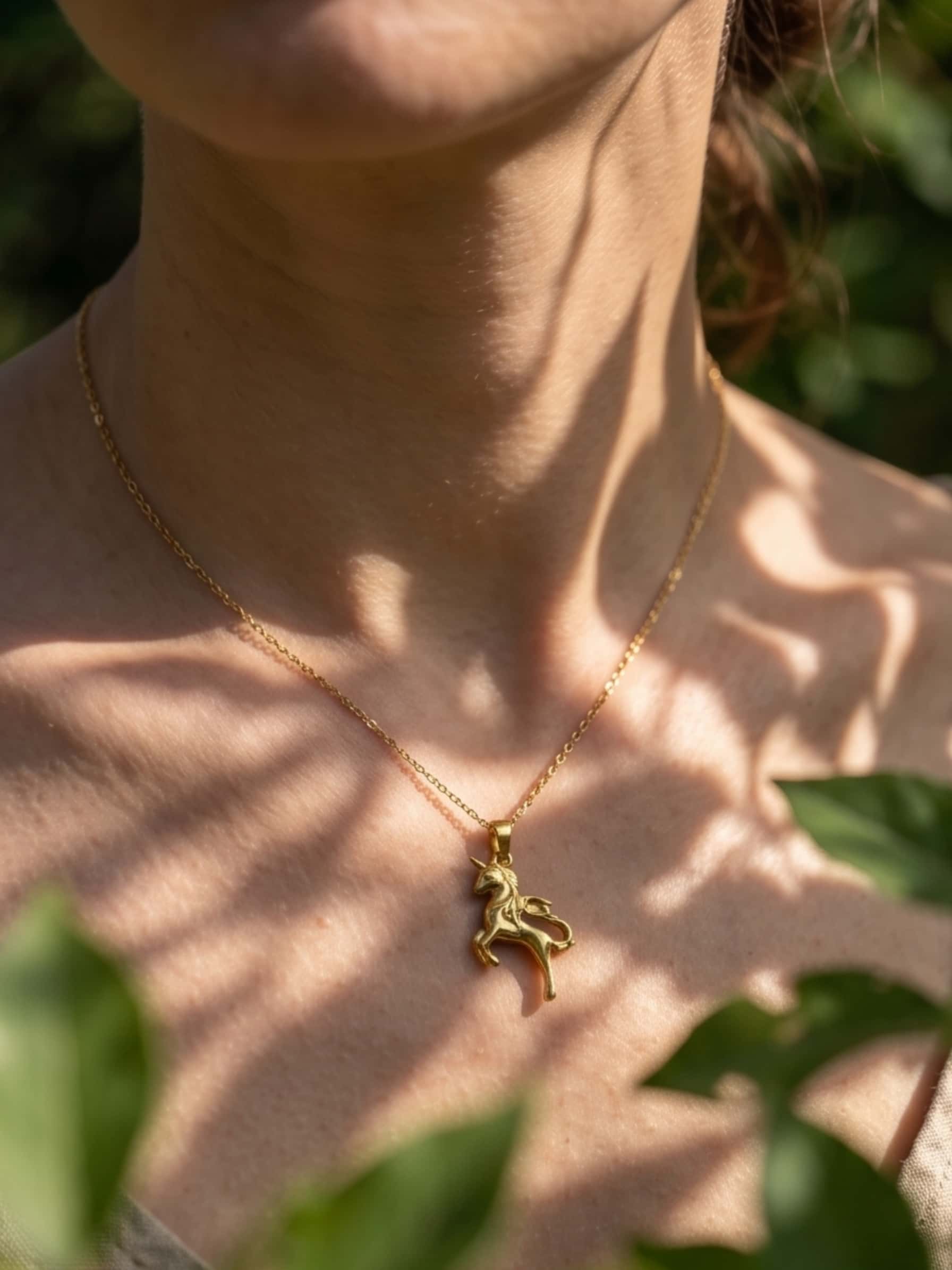 Aesthetic close-up of the unicorn necklace worn outdoors, highlighted by natural dappled leaf shadows