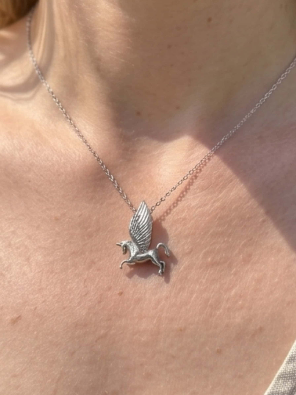 Close-up detail of an elegant unicorn necklace for adults worn elegantly around the neck, highlighting the silver craftsmanship in natural sunlight