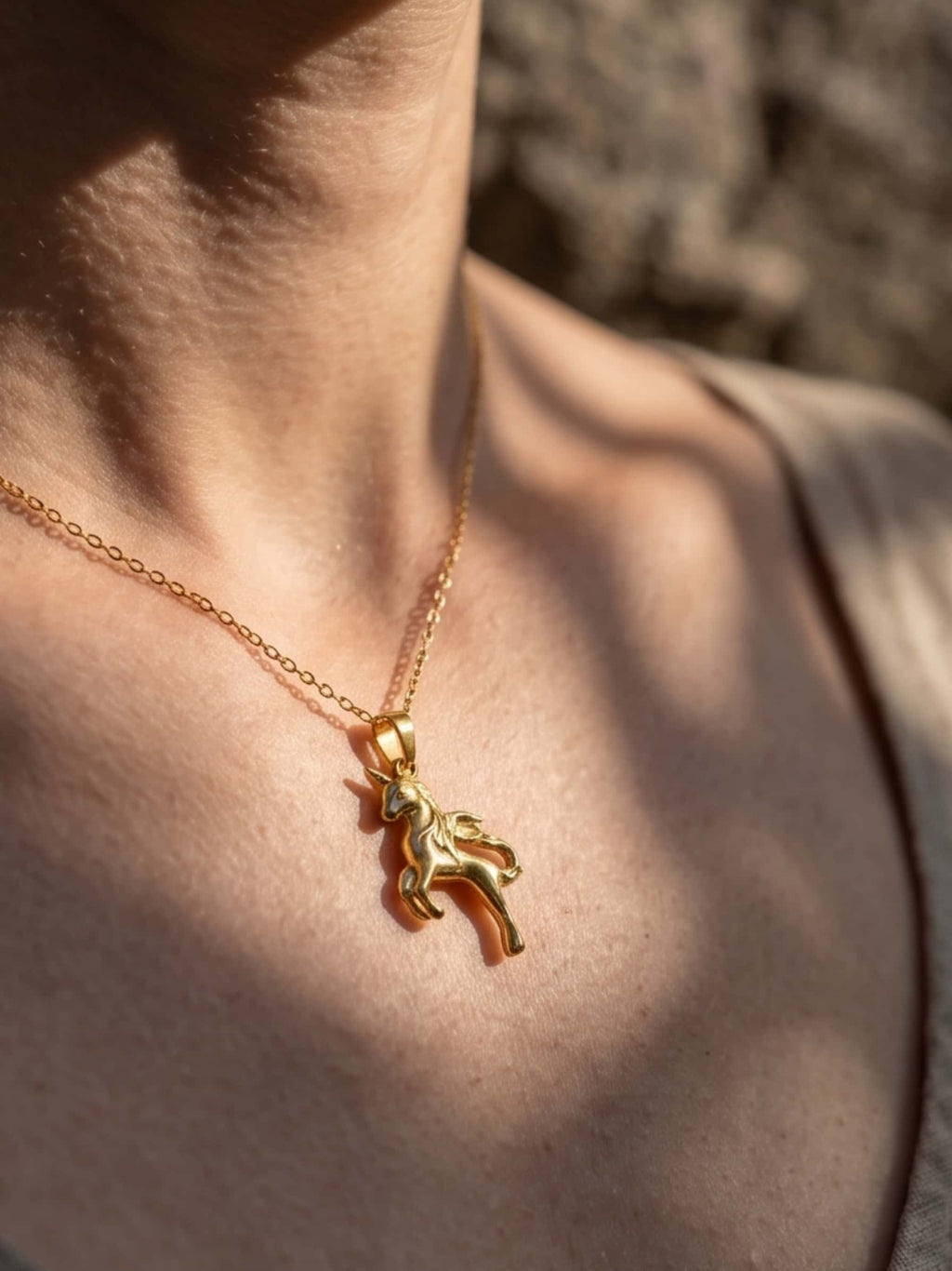 Close-up detail of the gold unicorn necklace for adults worn gracefully on the collarbone in natural sunlight