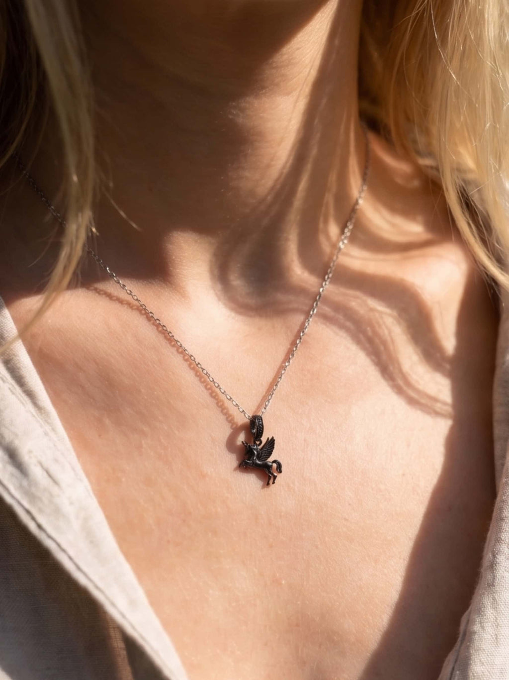 Close-up of a woman wearing the elegant black rhodium unicorn necklace for adults, highlighting the fine details of the winged unicorn pendant resting gently on her collarbone in natural sunlight
