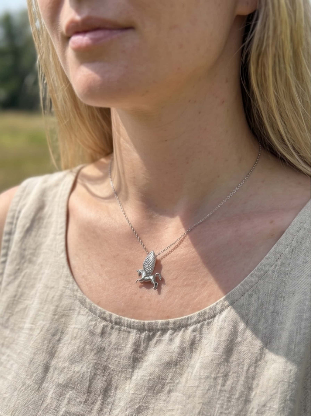 Blonde woman wearing a delicate unicorn necklace sterling silver outdoors, showcasing its proportions against a natural linen top