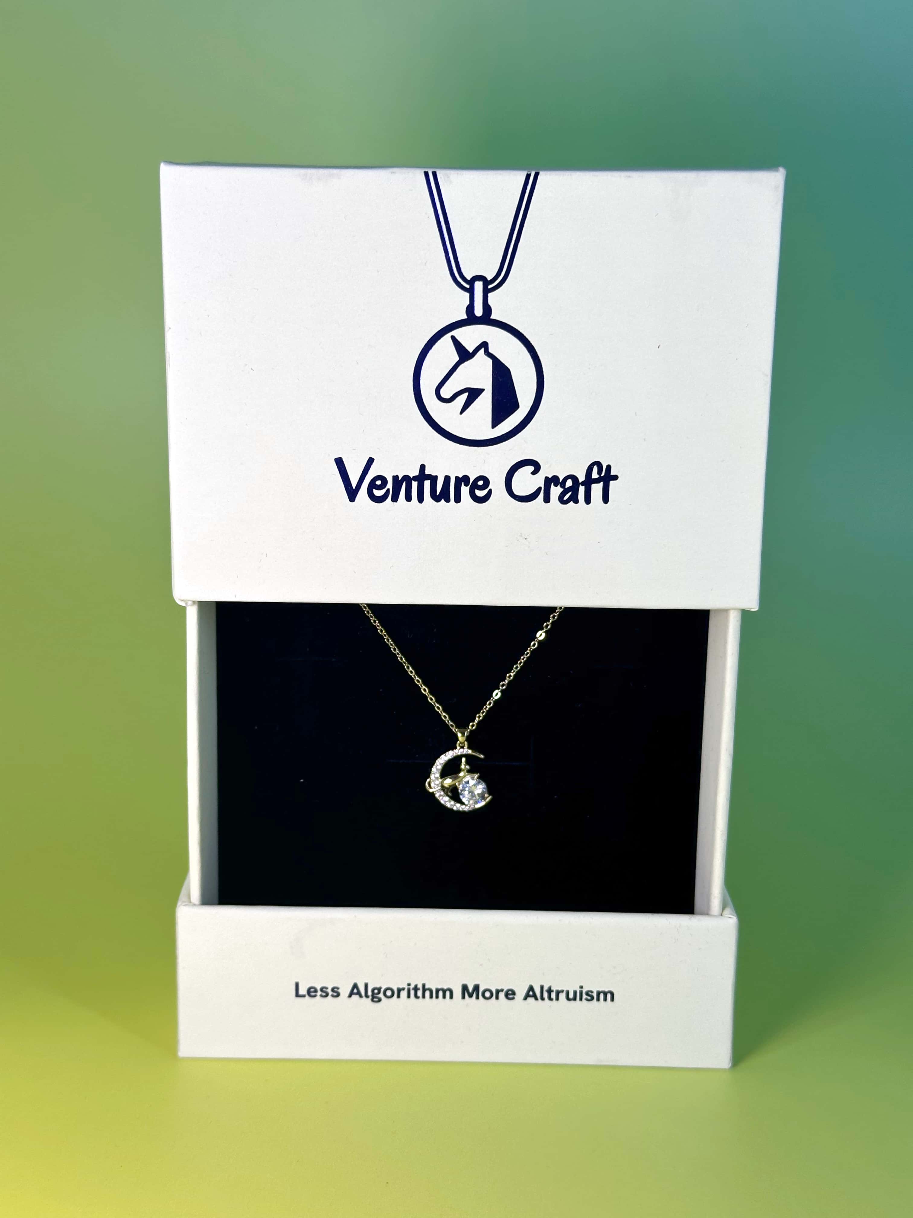 Premium white Venture Craft brand jewelry box open to reveal the gold cat pendant necklace on black velvet, featuring the warm brand philosophy text "Less Algorithm More Altruism"