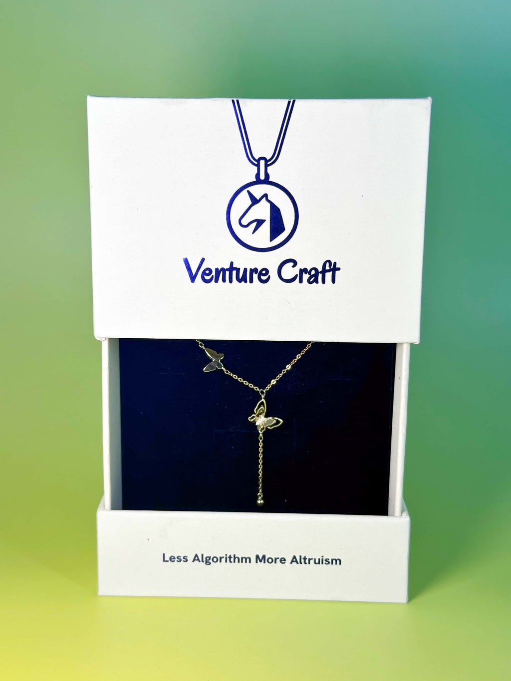 Premium white slide-out gift box packaging for the Venture Craft butterfly necklace, featuring a blue velvet display insert and the brand slogan Less Algorithm More Altruism