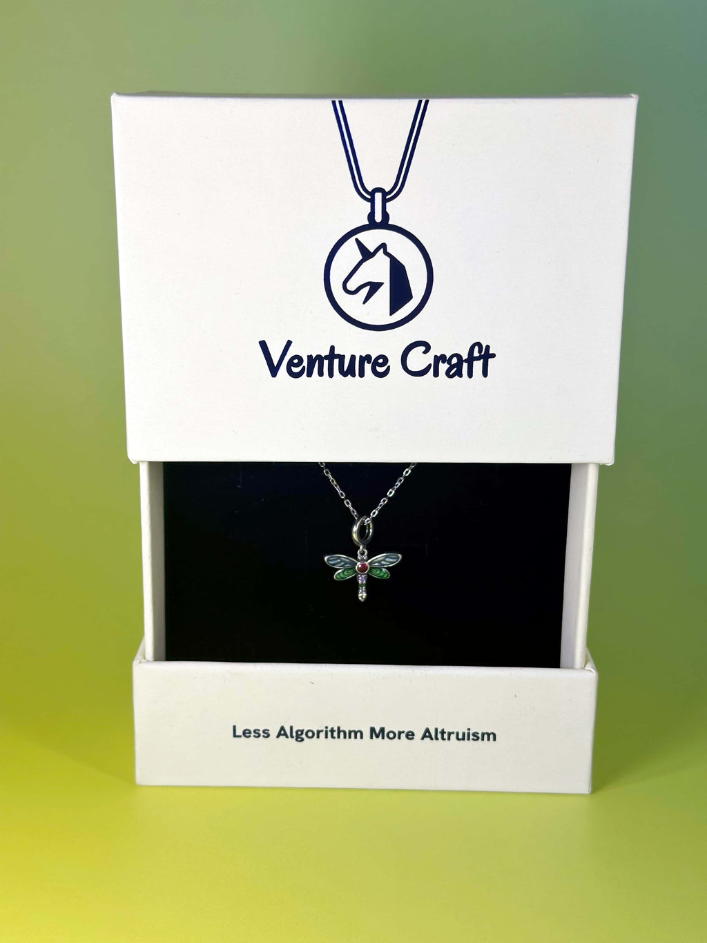 The sterling silver dragonfly necklace displayed beautifully inside a white Venture Craft branded jewelry gift box, featuring the slogan Less Algorithm More Altruism