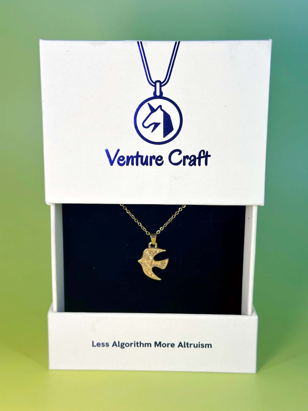 The elegant gold bird necklace displayed inside its white Venture Craft gift box featuring the brand tagline Less Algorithm More Altruism