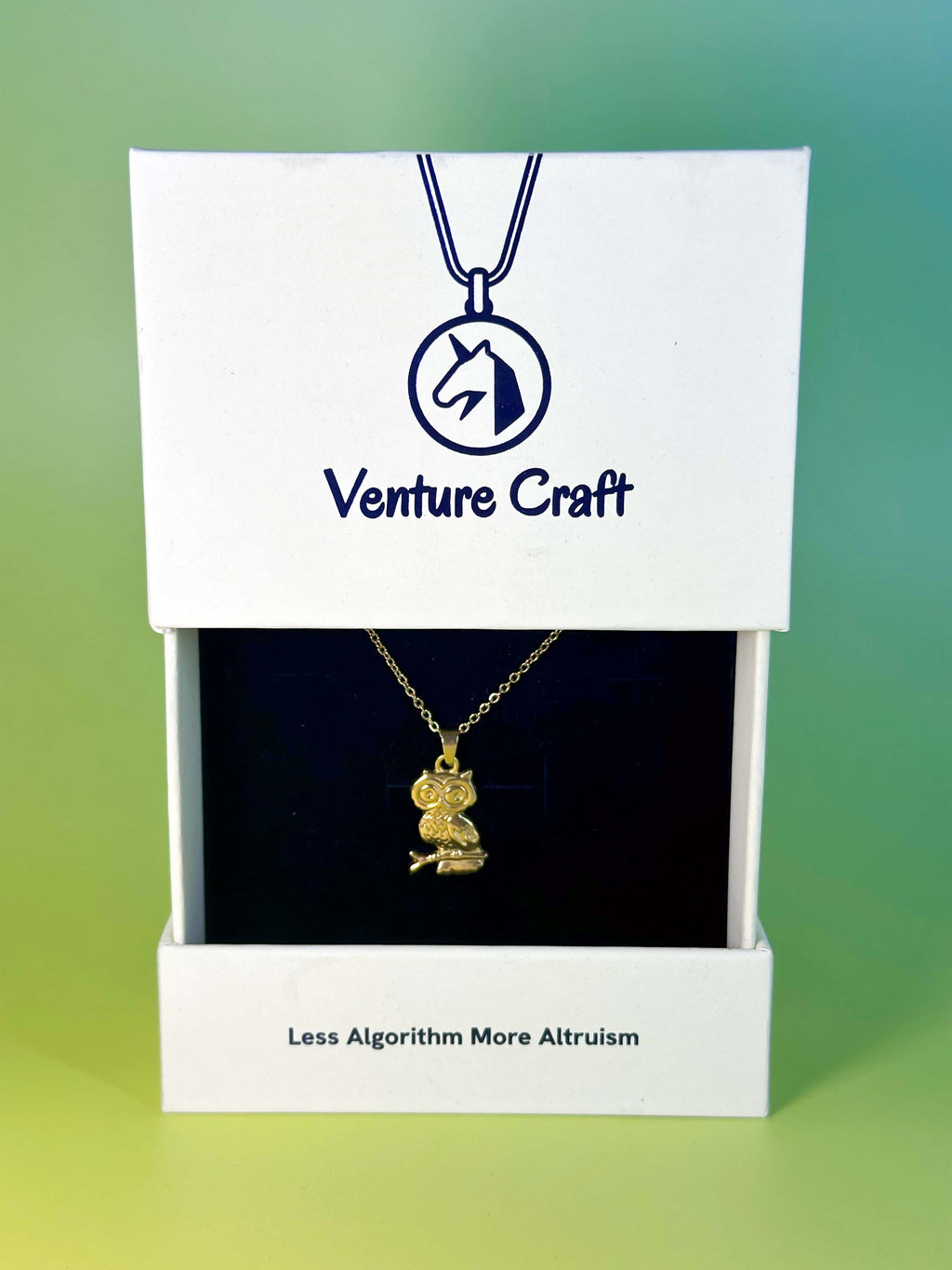 The gold owl pendant displayed inside its elegant white Venture Craft gift box featuring the brand slogan 'Less Algorithm More Altruism'