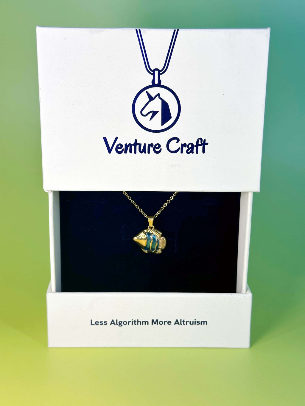The premium enamel fish necklace elegantly presented inside the white Venture Craft signature packaging box, printed with the brand philosophy Less Algorithm More Altruism