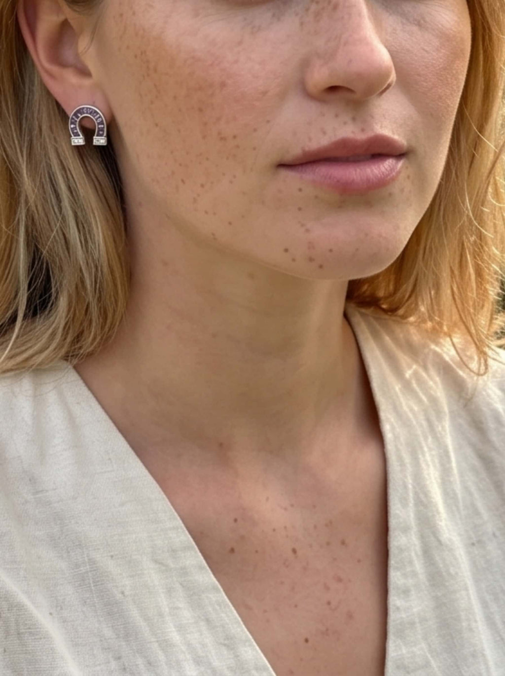 Mid-shot of a female model wearing a purple horseshoe earring paired with a casual lifestyle linen V-neck shirt