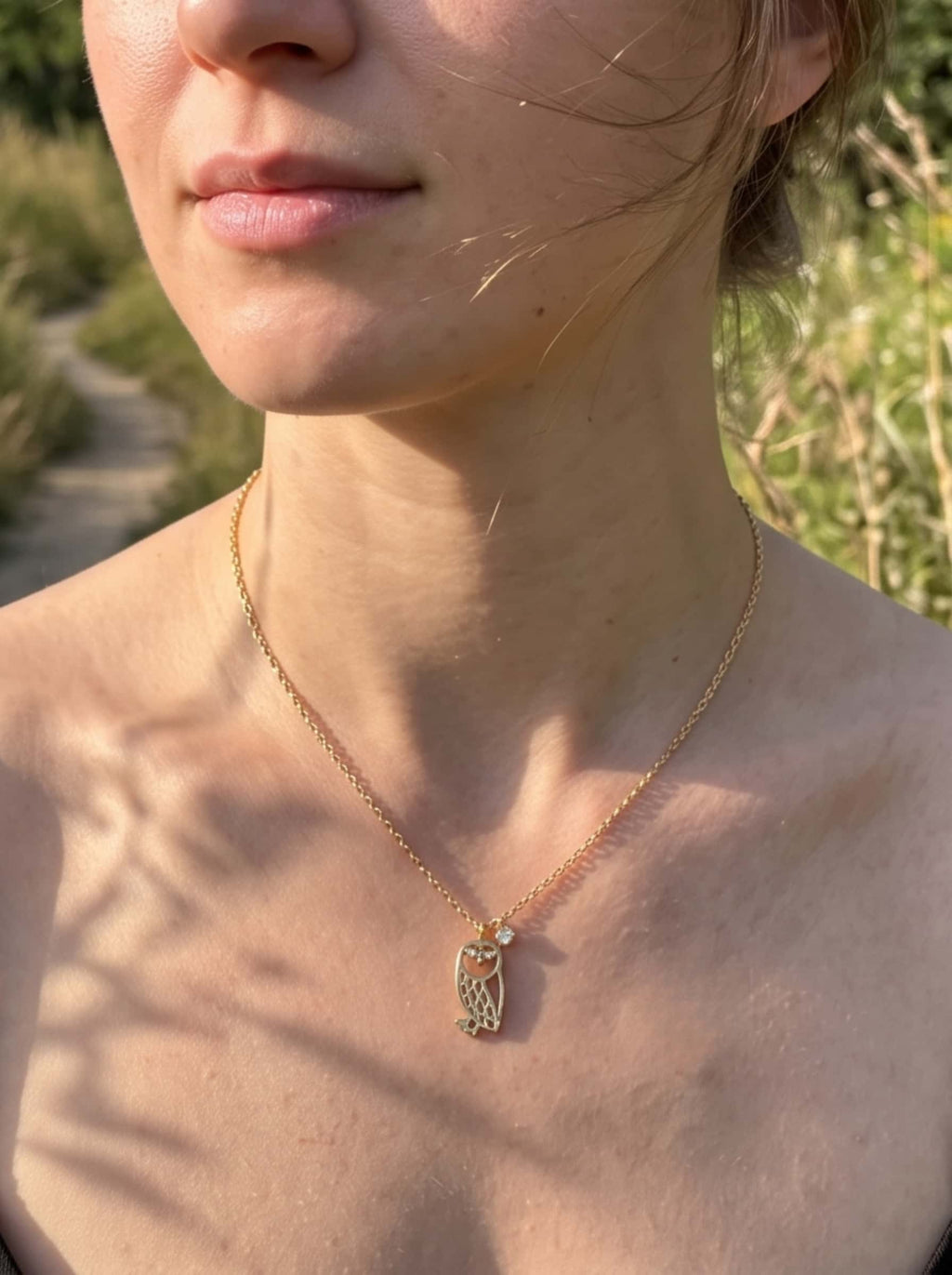 Woman wearing the 18K gold plated owl necklace outdoors in natural light, showing the drop length and styling on the neckline