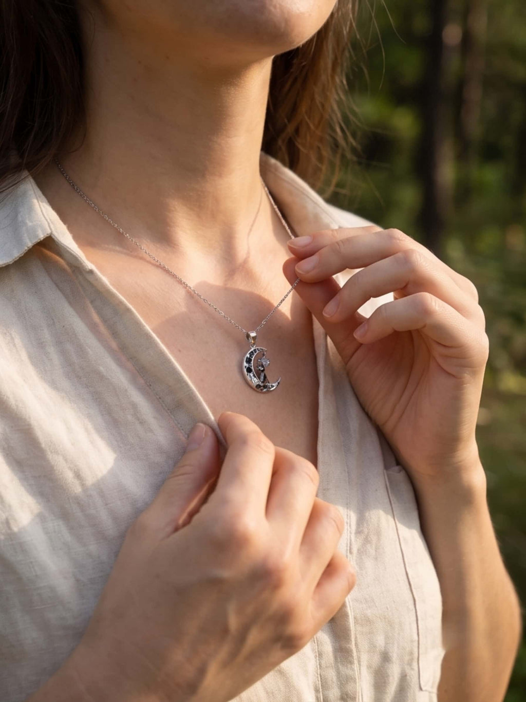 Close up of a woman's hands gently touching her elegant silver cat pendant outdoors in golden hour light
