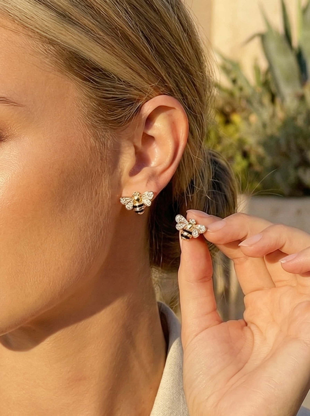 Close-up of a person wearing a gold bee earrings with a blurred outdoor background