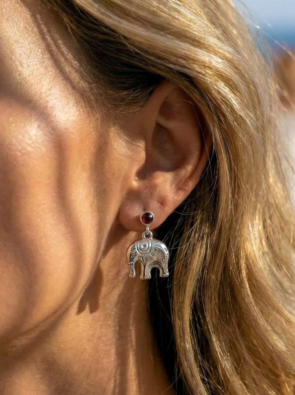 Close-up of an ear wearing a silver elephant earring with a dark gemstone.