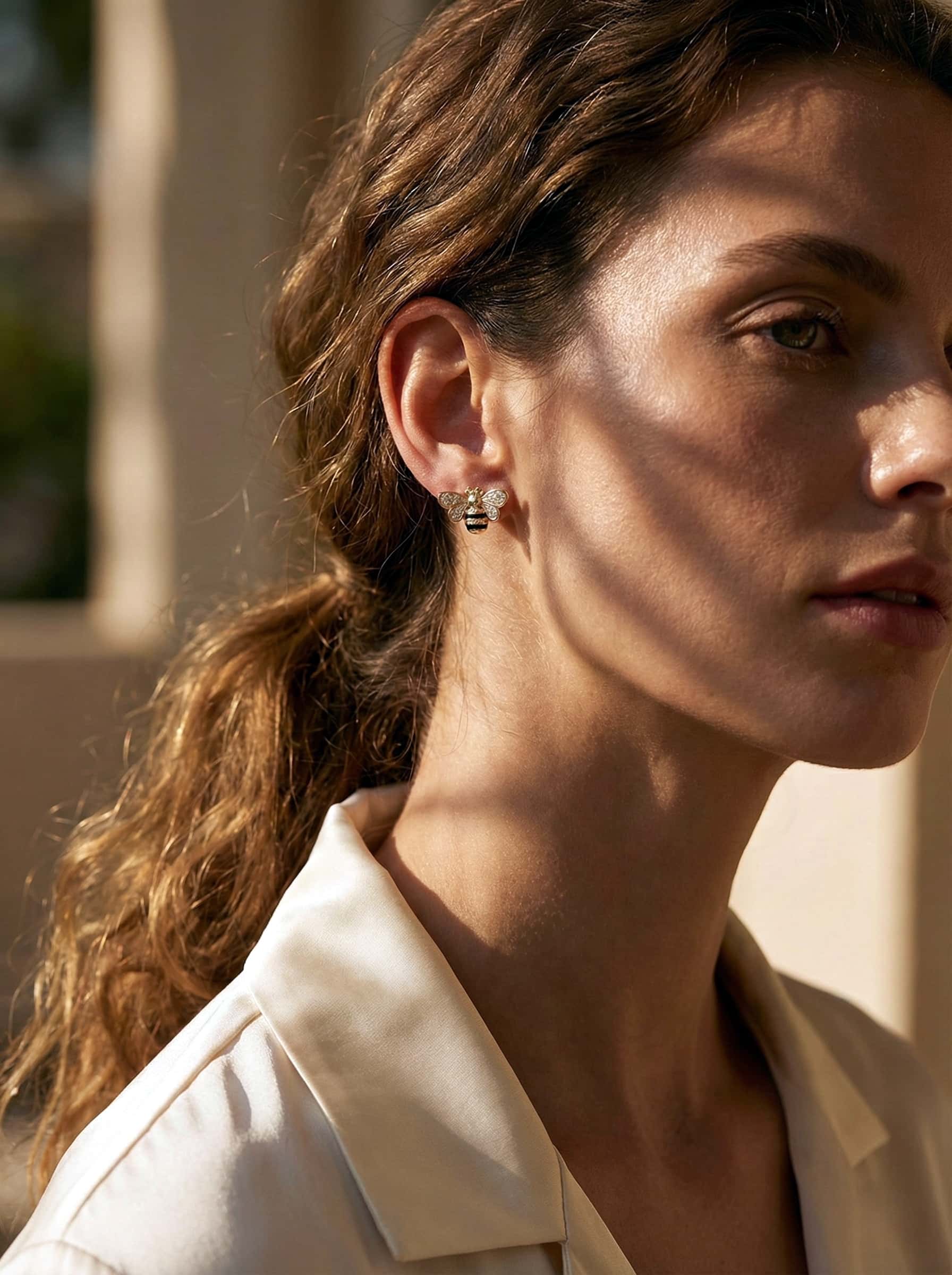 Close-up of a woman wearing bee  earrings with a blurred outdoor background
