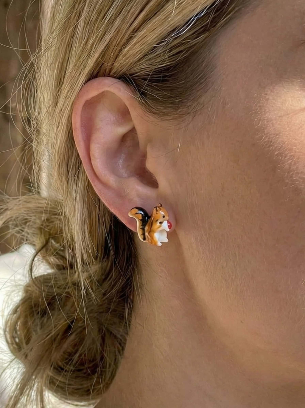 Close-up of an ear wearing a small squirrel earring with blonde hair.