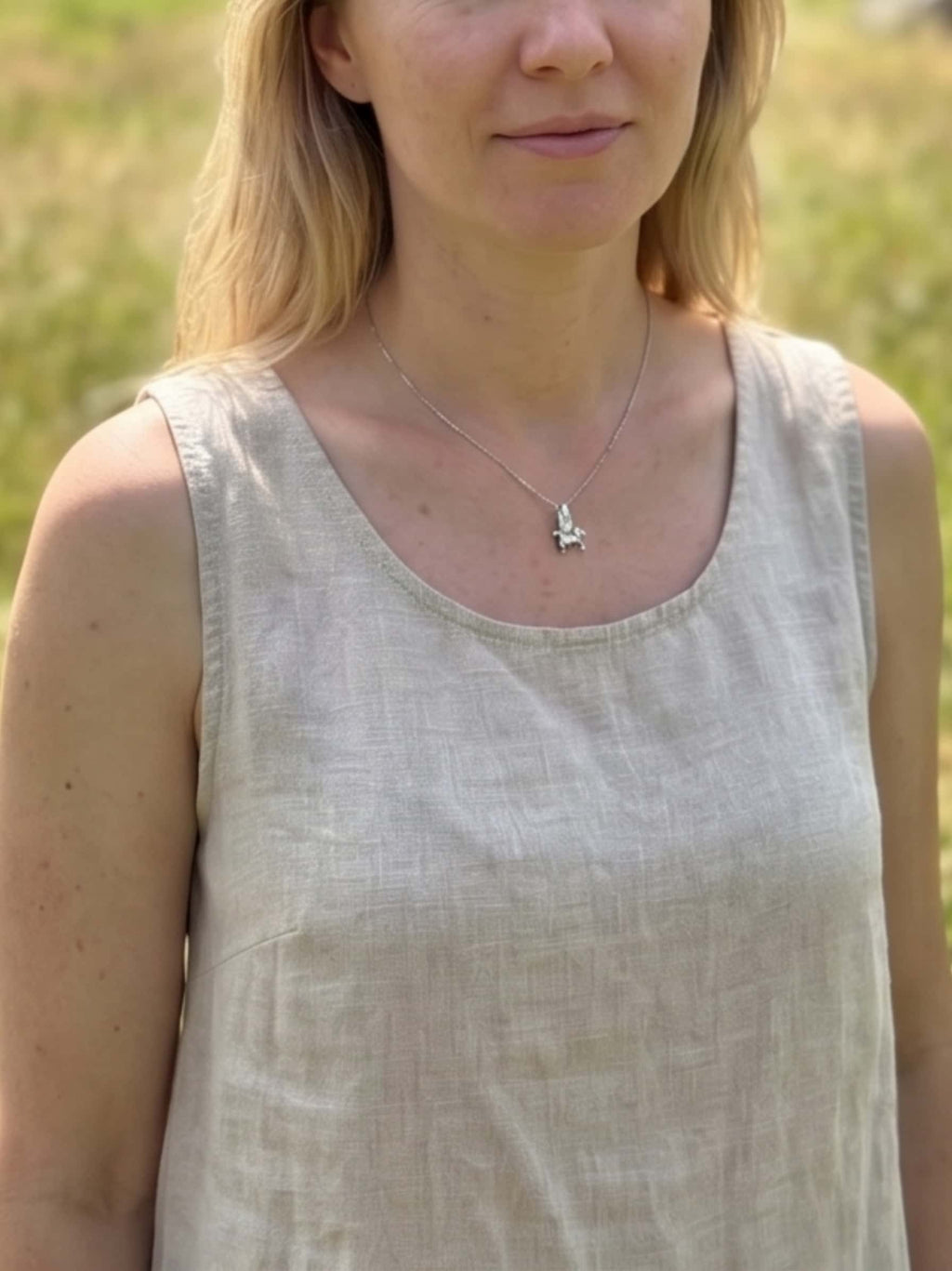 Medium lifestyle shot of a woman standing in a sunny field styling a premium sterling silver unicorn necklace