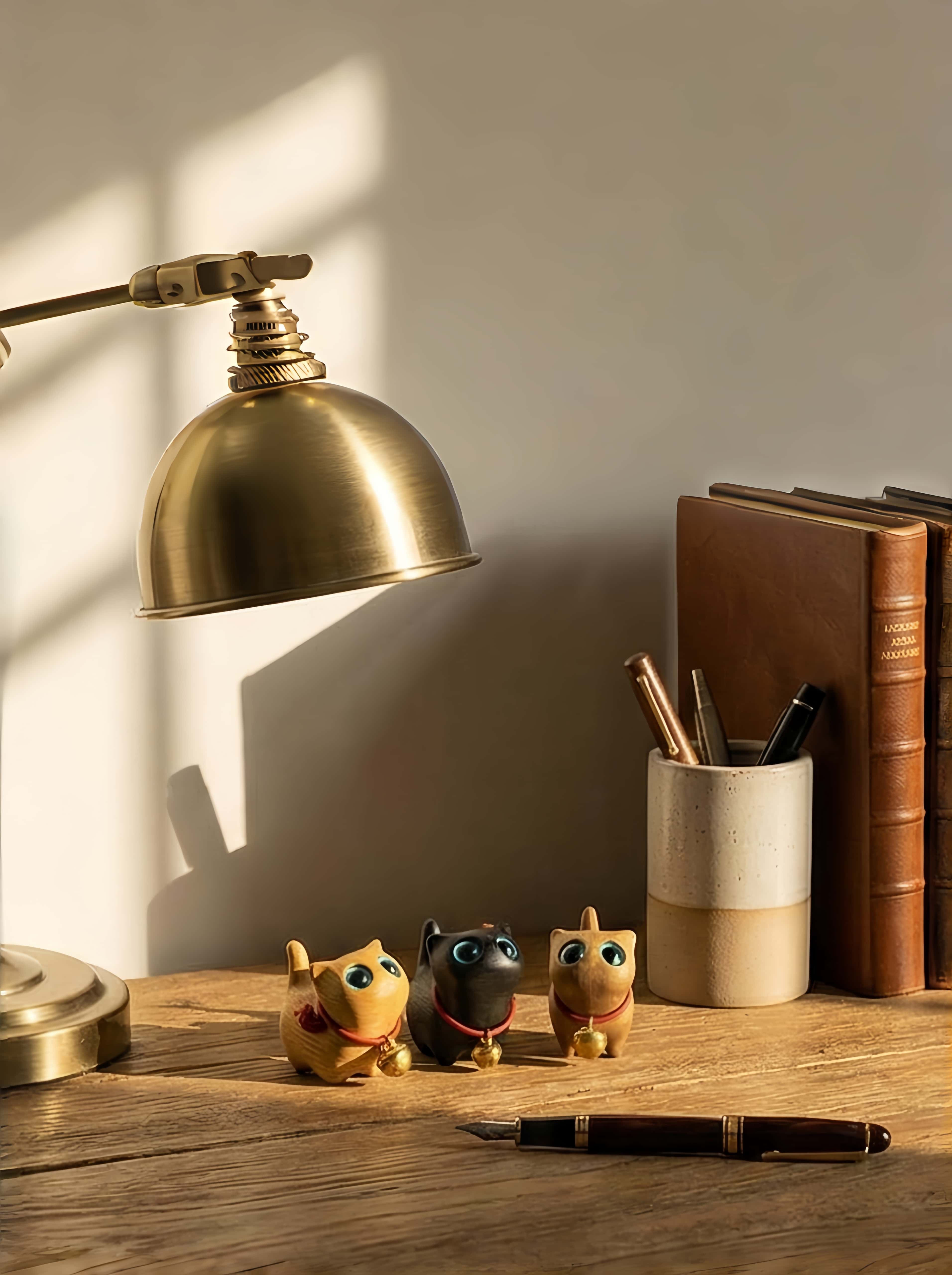 Gold lamp, 3 small wood sculpture cats, books, and a pen on a wooden surface with a neutral background.