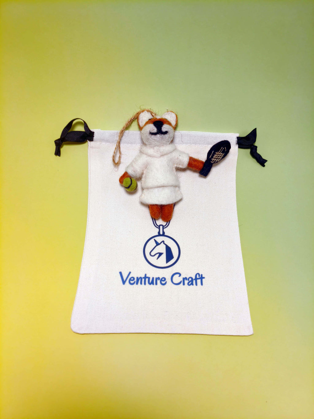 wool felt ornament fox resembling a fox with tennis rackets and ball on a Venture Craft branded drawstring bag.