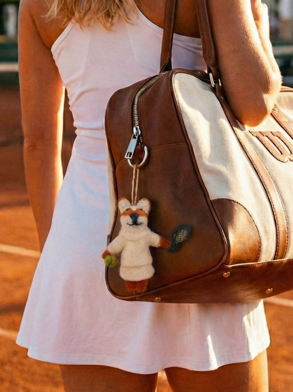 Person wearing a white dress holding a brown leather bag with a wool felt ornament fox on a blurred background