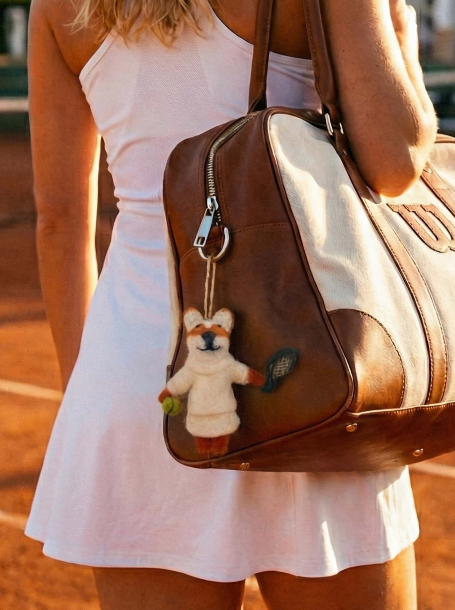 Person wearing a white dress holding a brown leather bag with a wool felt ornament fox on a blurred background