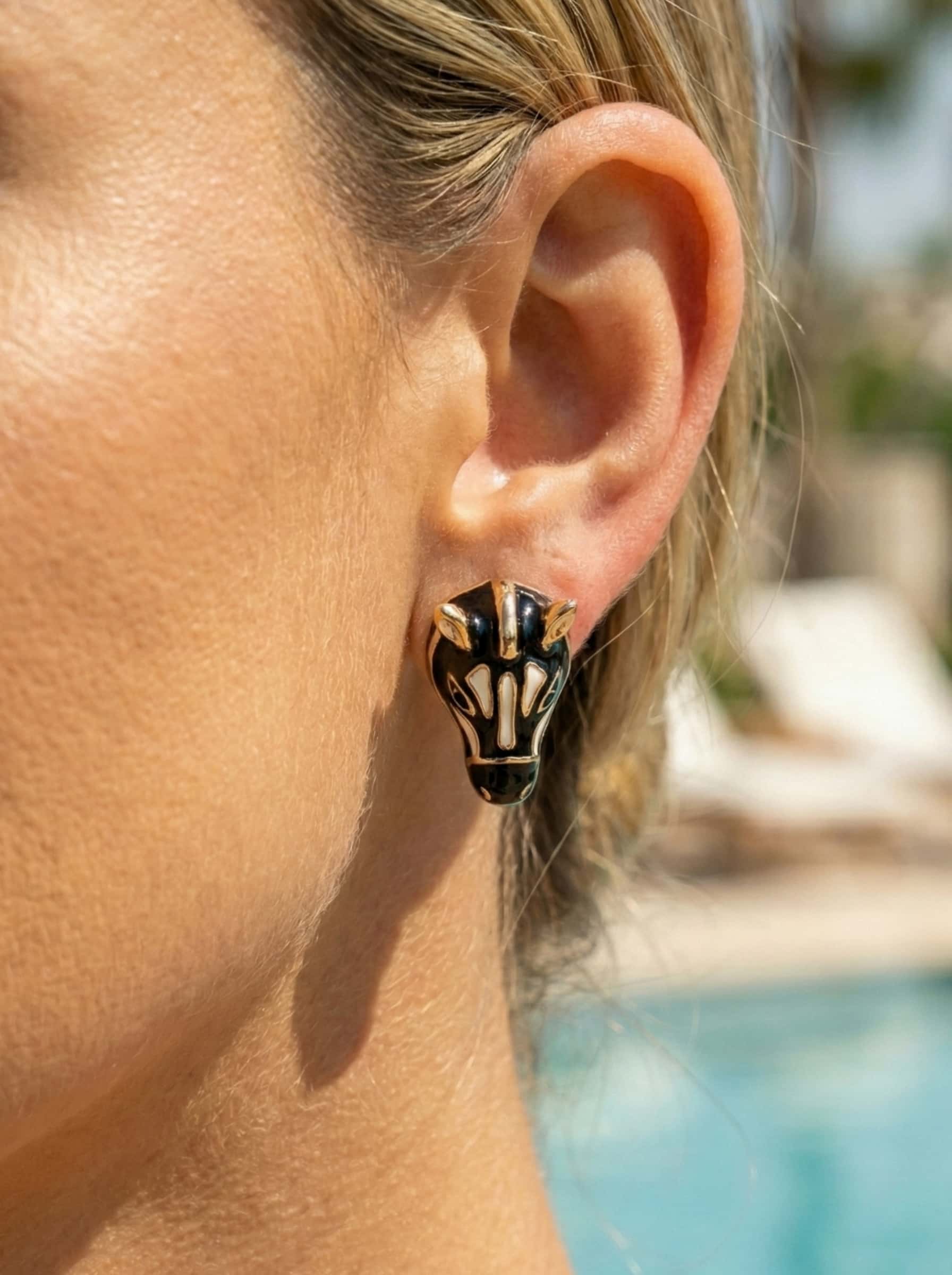Close-up of an ear wearing a decorative zebra-shaped earring with a blurred outdoor background